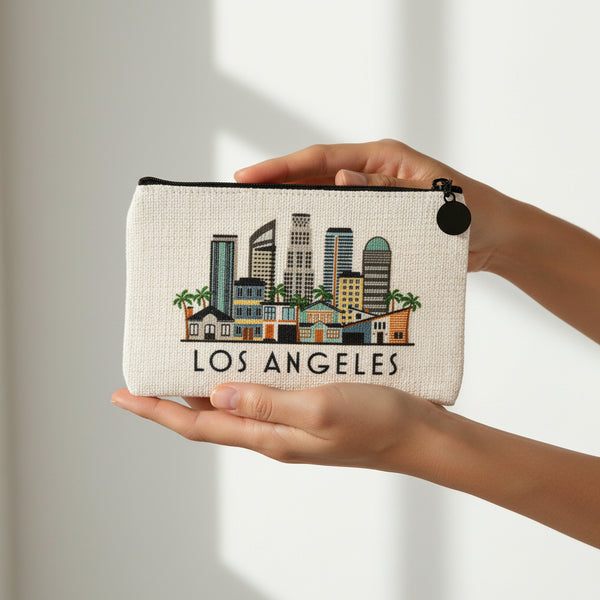 An off-white canvas zippered pouch featuring a colorful Los Angeles skyline illustration and the text 'LOS ANGELES' printed below, with a black zipper and black charm.