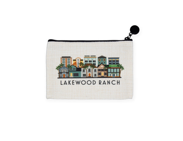 An off-white canvas zippered pouch featuring a colorful illustration of vintage houses and the text 'LAKEWOOD RANCH' below it, with a black zipper and black pom-pom pull.