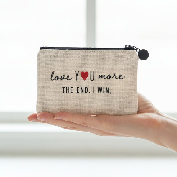 An off-white woven zippered pouch with black text reading 'love YOU more THE END. I WIN.