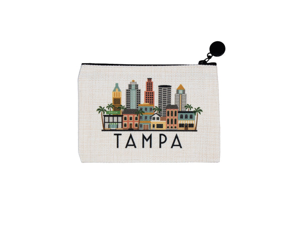 A small zip pouch with a black zipper and black pom-pom charm, featuring a colorful Tampa skyline illustration and the word 'TAMPA' printed below, on a white background.