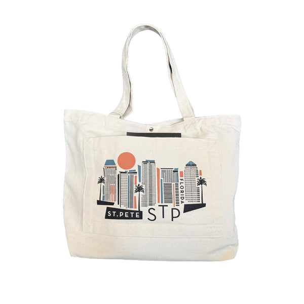 An off-white canvas tote bag featuring a front pocket printed with a stylized city skyline graphic and the text 'ST. PETERSburg STP' in black, with a small orange sun accent.